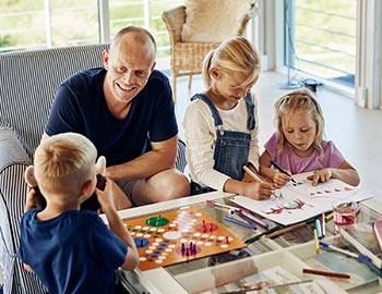 Far og børn spiller brætspil og tegner i sommerhus
